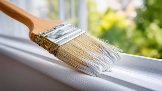 A paintbrush applying white, glossy paint to a window trim at Red Star Paint near Montclair, NJ